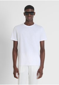 Camiseta blanca de manga corta con cuello redondo. Presenta un pequeño logo en relieve en el pecho. Textura suave y lisa, y corte regular.