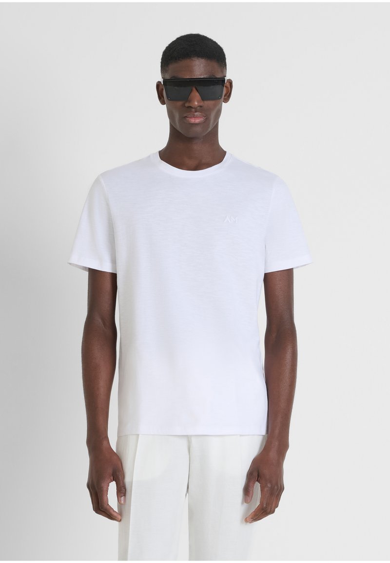 Camiseta blanca de manga corta con cuello redondo. Presenta un pequeño logo en relieve en el pecho. Textura suave y lisa, y corte regular.