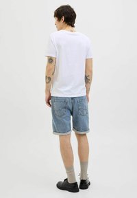 White cotton t-shirt, light blue denim shorts, rolled hems, worn look, black shoes, grey socks, and visible tattoos on forearms.