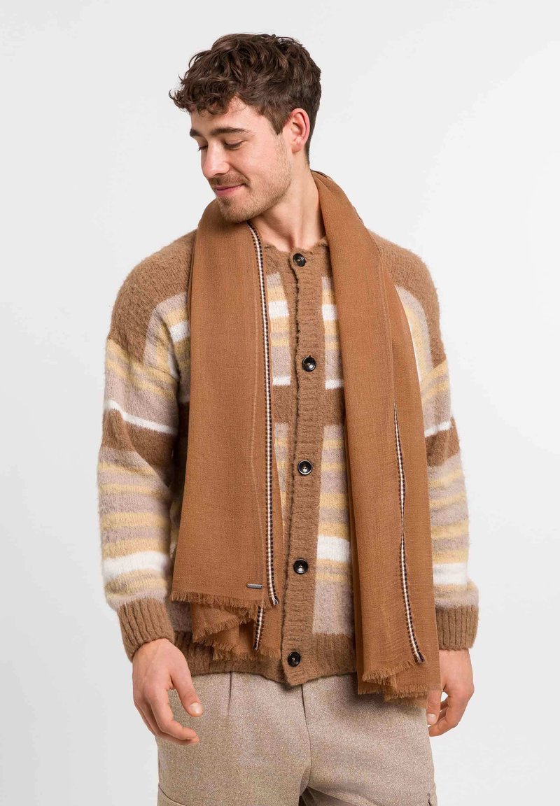 Cardigan de punto marrón a rayas con botones negros, acompañado de una bufanda marrón sólida con flecos. Texturas suaves y una paleta de colores cálidos.