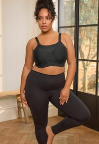 Zwarte beha en high-waisted leggings gemaakt van zacht, rekbaar materiaal. De beha heeft een naadloos ontwerp met brede banden voor ondersteuning.