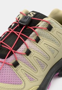 Scarpa da trail leggera con tomaia in rete beige e rosa, con dettagli neri, lacci elastici e suola in gomma testurizzata.