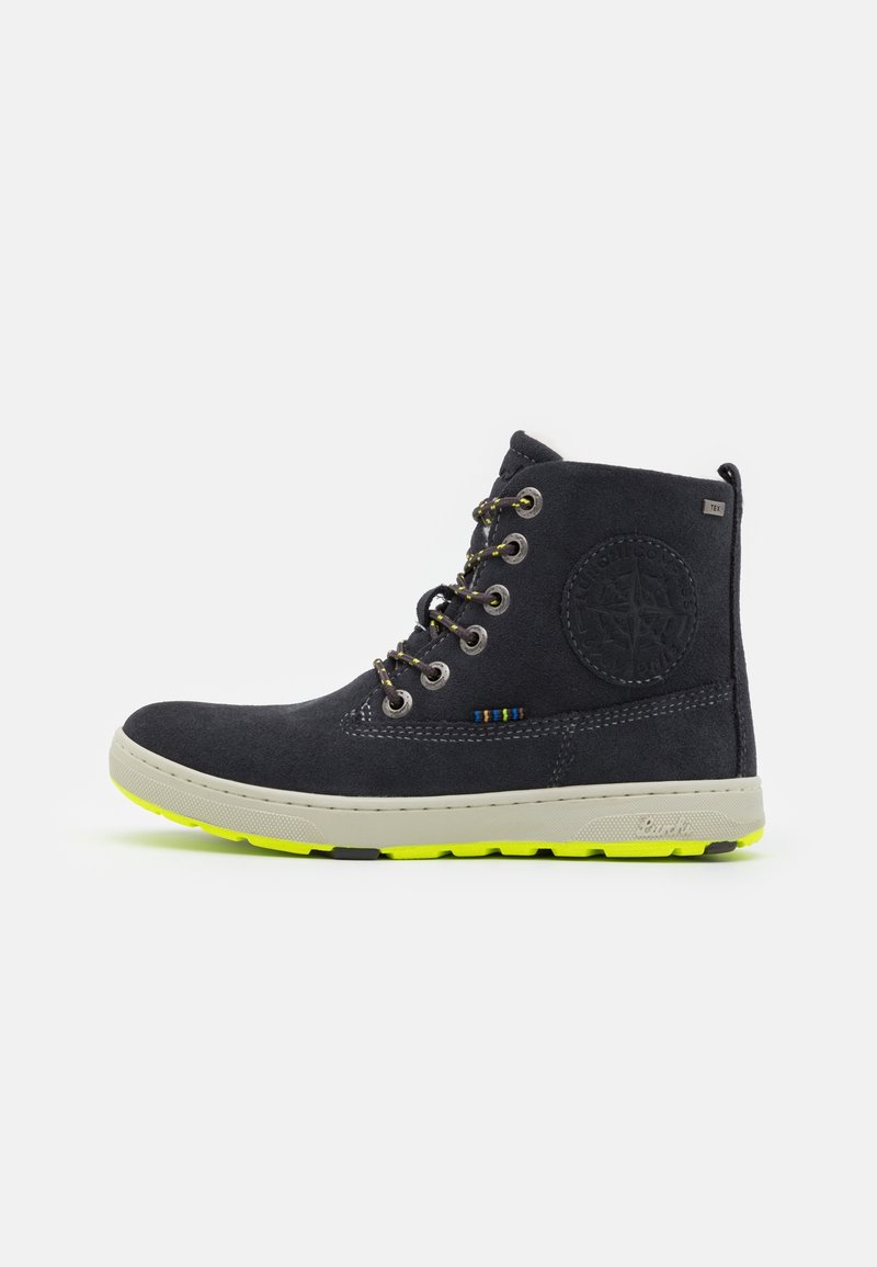 Botte montante en daim noir avec lacets à accents jaunes, écusson rond avec logo, semelle beige et bande de roulement jaune fluo sur fond blanc.