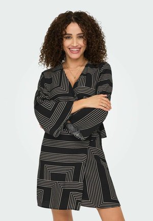 Abito nero con linee geometriche bianche, design avvolgente, maniche lunghe, scollo profondo e una fessura laterale. Tessuto liscio con una leggera lucentezza.