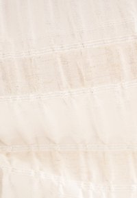 Tissu crème transparent avec un motif texturé, présentant de subtiles rayures horizontales et des accents de couture délicats.