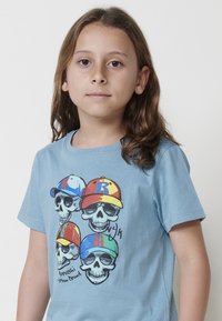 Camiseta de algodón azul claro con un gráfico de cuatro calaveras que llevan gorras coloridas, con un texto impreso en la parte inferior que dice "Koroshi Urban Brand."