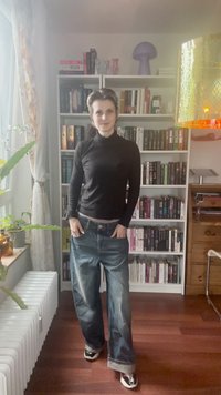 Fekete, hosszú ujjú garbó, laza kék farmernadrággal, amely cipzárral és gombbal záródik. A szettet fekete-fehér sportcipők egészítik ki.