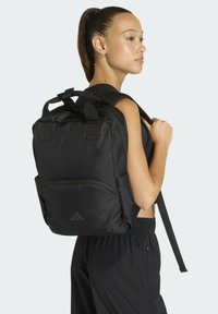 Zaino nero realizzato in tessuto resistente, con spallacci regolabili, maniglia superiore e una tasca frontale con cerniera e un logo discreto.