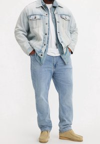 Chaqueta de mezclilla azul claro con botones oscuros, dos bolsillos en el pecho, combinada con jeans azul claro y zapatos beis sin cordones. Camiseta blanca debajo.