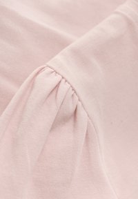 Ljusrosa tyg med rynkade detaljer längs sömmen, som visar en mjuk textur och slät yta. Lämpligt för olika kläddesigner.