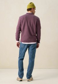 Paarse trui met lange mouwen, ronde halslijn, gelaagd over een wit gestreept shirt. Draag het met lichtblauwe jeans en een groene beanie.