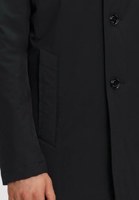 Schwarzer Mantel mit glatter Oberfläche, Knopfverschluss und einer Seitentasche. Der Stoff wirkt leicht und hat ein elegantes Design.