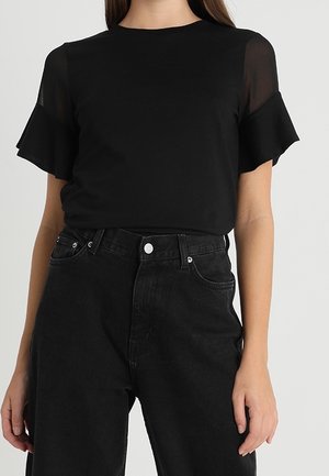 Sort T-shirt med korte, gennemsigtige flæseærmer, rund halsudskæring, kombineret med højtsiddende sorte jeans med knaplukning og sidelommer.