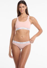 Lichtroze sportbh met brede bandjes en het Guess Jeans-logo op een witte band, gecombineerd met bijpassende lichtroze bikini-achtige onderbroeken.