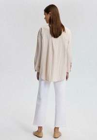 Light beige, striped shirt with a loose fit, long sleeves, and a round hem, paired with white cropped pants and beige slip-on shoes.