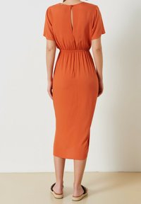 Měděně oranžové midi šaty s krátkými rukávy, elastickým pasem a detailem klíčové dírky na zádech. Měkká tkanina s hladkou texturou, bez viditelných vzorů.