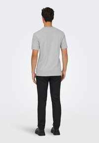 Γκρι βαμβακερό μπλουζάκι με στρογγυλό ντεκολτέ, κοντά μανίκια και ίσιο τελείωμα, φορεμένο με μαύρο παντελόνι και μαύρα παπούτσια. Εμφανίζεται η πίσω όψη.