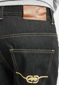 Mustad denim teksad musta värviga ja nähtava kuldsete õmblustega. Vöökoht on varustatud nahklabeliga, millel on sisse pressitud bränd.