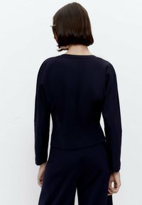 Blusa blu navy con maniche lunghe e scollatura arrotondata, caratterizzata da un design aderente e una texture liscia, vista da dietro.