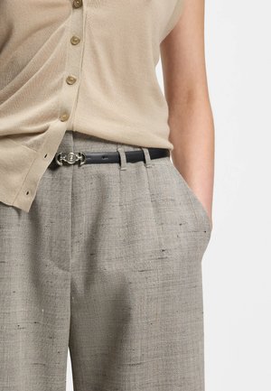 Top beige senza maniche con bottoni, infilato in pantaloni grigi a vita alta con trama, completati da una cintura nera con fibbia argentata.