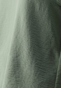 Tela verde claro, texturizada con arrugas sutiles; superficie suave, apariencia delicada, brillo mínimo, drapeada con suaves pliegues.