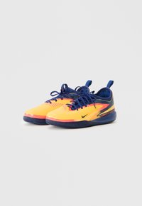 Dzelteni un tumši zili sporta apavi ar auklām un nelielu melnu Nike logo, novietoti blakus uz vienkārša fona.