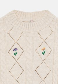 Suéter em creme de malha com textura de ponto de cabos, padrões em diamante e flores bordadas em roxo e amarelo com folhas verdes.