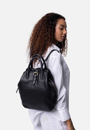 Zaino in pelle nera con doppi manici, una fibbia in metallo dorato e una tasca con zip sul lato. Texture morbida e forma strutturata.