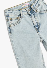 Pantalones vaqueros para niños de mezclilla azul claro con diseño acampanado, que cuentan con detalles desgastados, estilo de cinco bolsillos y costuras amarillas en contraste.