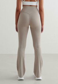 Beige utsvängda leggings gjorda av sträckt material, med hög midja och slät textur, tillsammans med kontrasterande vita skor.