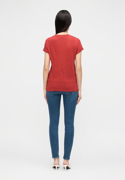 T-shirt vermelha de manga curta com corte relaxado, combinada com jeans azuis de corte justo e saltos bege. O material parece macio com poucos detalhes.