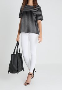 Top a righe bianche e nere con maniche corte, abbinato a jeans skinny bianchi. Una borsa a tracolla nera texturizzata con borchie e sandali neri con tacco.