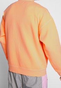 Sweatshirt oversize di un vivace arancione, con una texture morbida, polsini a coste e un orlo dritto. Design minimalista senza loghi visibili.