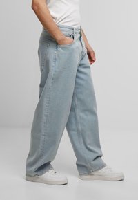 Helle blaue weit geschnittene Jeans mit hoher Taille, ausgestattet mit Fronttaschen und einem Reißverschluss. Kombiniert mit weißen Sneakern.