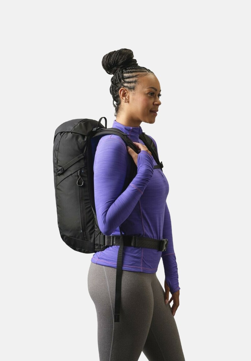 Sac à dos noir avec bretelles rembourrées et ceinture abdominale, porté par une personne vêtue d'un haut à manches longues violet, sur fond blanc.