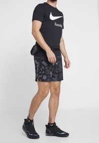 Camiseta negra de Nike con logo blanco, pantalones cortos negros estampados con varios gráficos y zapatos deportivos negros con acentos reflectantes.