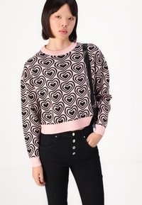 Schwarzer und rosa kurzer Pullover mit Herzmuster, geripptem Kragen und Bündchen, kombiniert mit schwarzen hochtaillierten Hosen mit Knopfdetails.