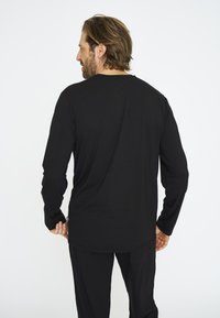 Langærmet sort t-shirt lavet af blødt bomuld. Har en rund halsudskæring, afslappet pasform og et lille logomærke nederst til venstre.