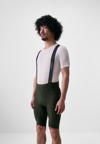 Fietsoutfit met een witte mesh korte mouwen basislaag en donkergroene high-waisted shorts met zwarte bretels en padding.