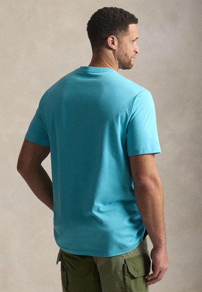 Βαμβακερό μπλουζάκι τυρκουάζ με κοντά μανίκια, στρογγυλή λαιμόκοψη, άνετη γραμμή, ορατές ραφές, συνδυασμένο με χακί cargo παντελόνι.