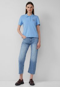 Svetlo modra polo majica s kratkimi rokavi, gumbasto zapiranje in logotipom. V kombinaciji s svetlo modrimi skrajšanimi kavbojkami in temno rjavimi loaferji.