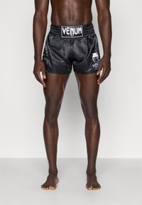 Pantalones cortos deportivos de satén negro con cintura elástica, con la marca "Venum" en blanco en la parte frontal. Textura suave y corte ajustado.