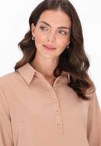 Beige Bluse mit Kragen, zwei Knöpfen und langen Ärmeln. Weiches, glattes Material mit subtiler Satinoptik und ohne sichtbare Muster oder Akzente.