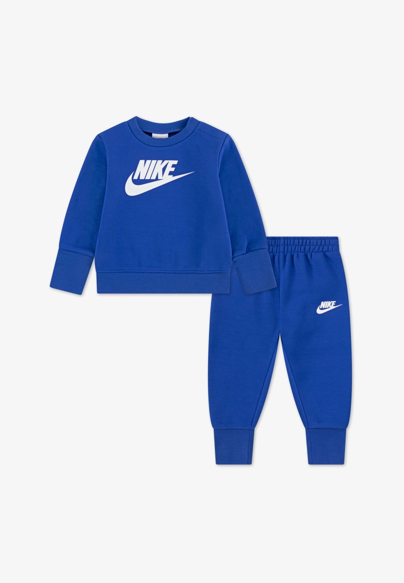 Set albastru de bluză și pantaloni Nike. Bluză cu decolteu rotund și logo alb Nike; pantaloni cu talie elastică și manșete conice.