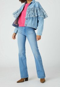 Světle modrá džínová bunda s třásněmi, pod kterou je výrazná růžová mikina, doplněná světle modrými rozšířenými d�žínami a hnědými botami na podpatku.