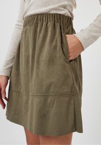 Olivengroene suede rok met een elastische tailleband, zijzakken en een uitlopende zoom met gestikte accenten voor extra detail.