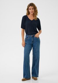 Marineblå plisseret top med korte ærmer kombineret med højtaljede, brede blå jeans. Jeans har sidelommer og dekorative sømme.