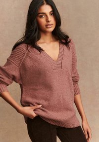 Übergroßer, strukturierter Pullover in Mauve mit tiefem V-Ausschnitt und gerippten Bündchen, der dezente Schimmerdetails im gesamten Material aufweist.