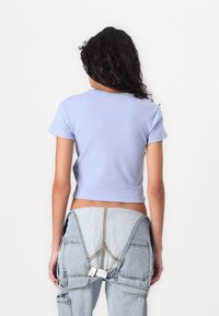 Světle modrý žebrovaný crop top s krátkým rukávem, s jednoduchým kulatým výstřihem a přiléhavým střihem, doplněný o džíny.