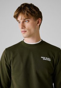 Donkergroen sweatshirt met een ronde hals, voorzien van een witte "RED BULL RACING" logo op de linkerkant van de borst.